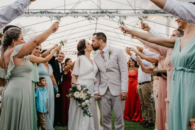 A newlywed couple kissing as wedding guests celebrate around them